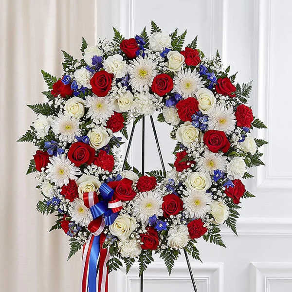Heart-shaped floral wreath with red, white, and blue flowers on a stand