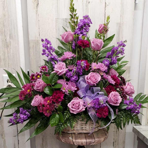 Pink and purple floral arrangement in a wicker basket on a wooden stand