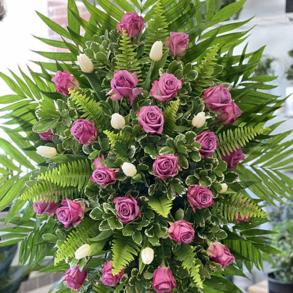 Standing floral spray with pink roses and white tulips surrounded by palm fronds