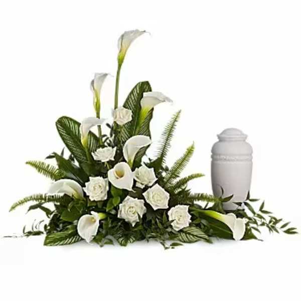 White funeral floral arrangement with calla lilies and roses beside an urn