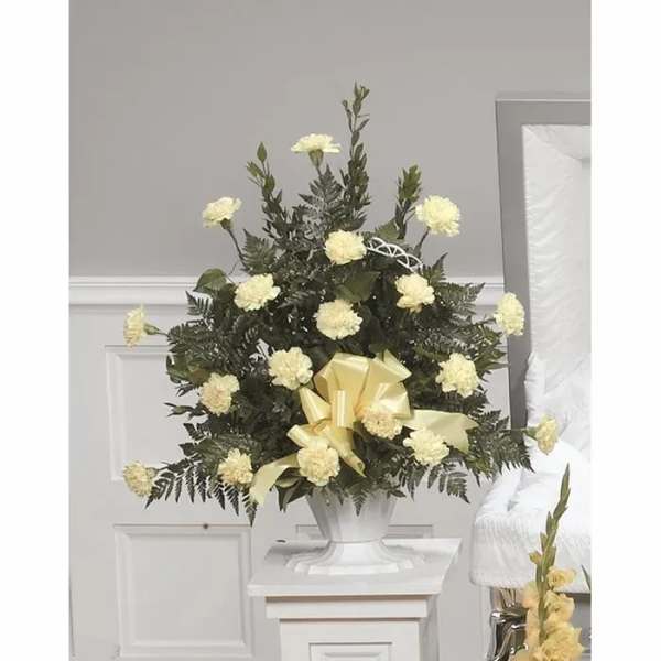 White carnation funeral spray with a yellow ribbon in a white urn