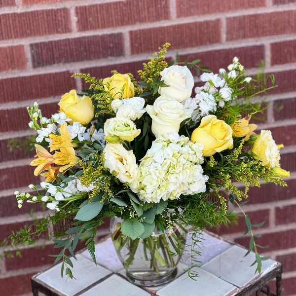 Yellow and white roses in a clear glass vase with mixed greenery