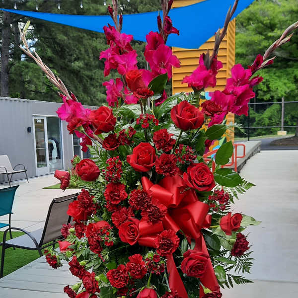 Tall red floral standing arrangement with roses and gladiolus on a metal easel