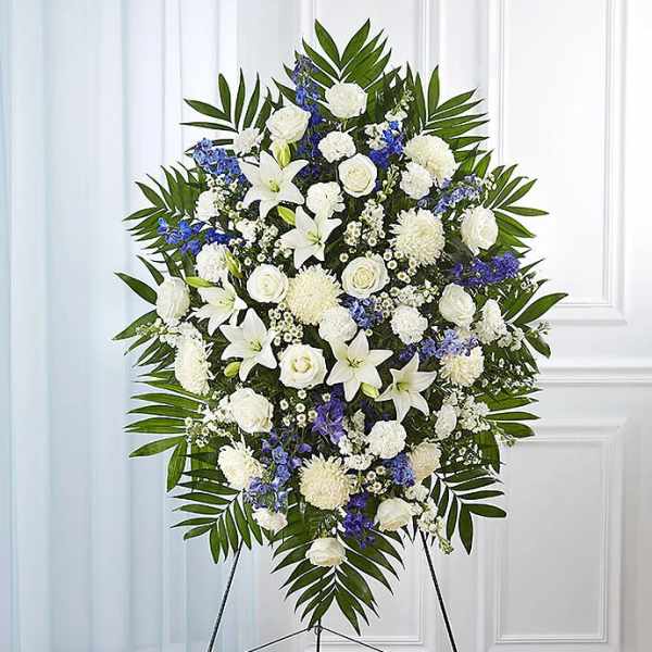White and blue funeral spray on a stand with palm leaves