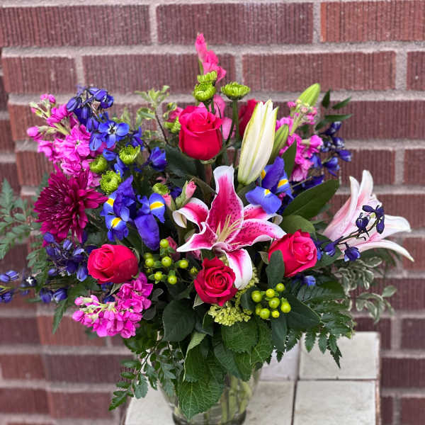 Mixed bouquet of pink roses, lilies, and blue flowers in a glass vase