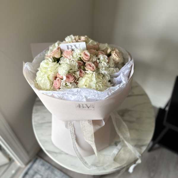 Bouquet of pale pink roses and white hydrangeas wrapped in blush paper