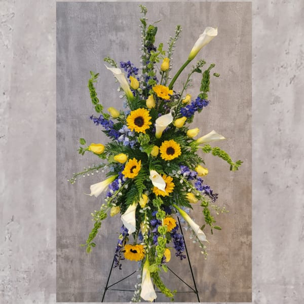 Tall standing arrangement with sunflowers, white calla lilies, and blue flowers