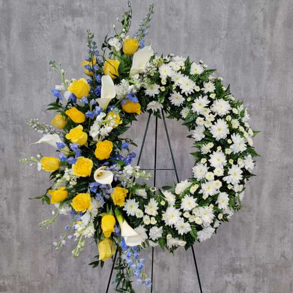 Floral wreath with yellow roses, white calla lilies, and white daisies on a stand