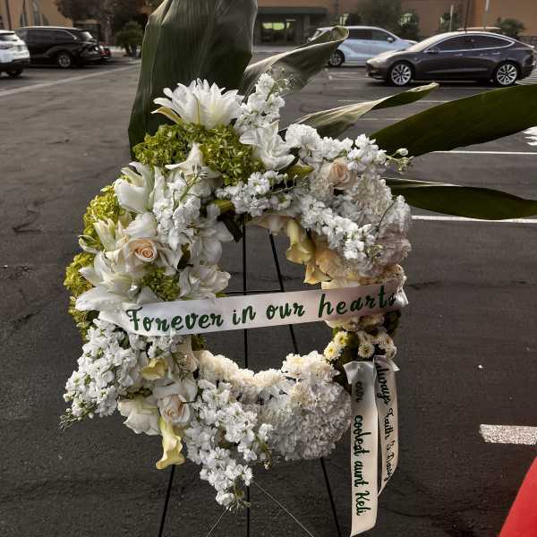 White floral wreath on an easel with a memorial ribbon