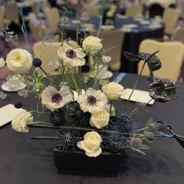 Modern floral centerpiece with white blooms and dark spiky accents in a black vase