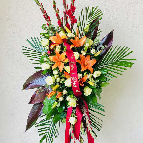 Standing floral spray with orange lilies and white roses on a red ribbon