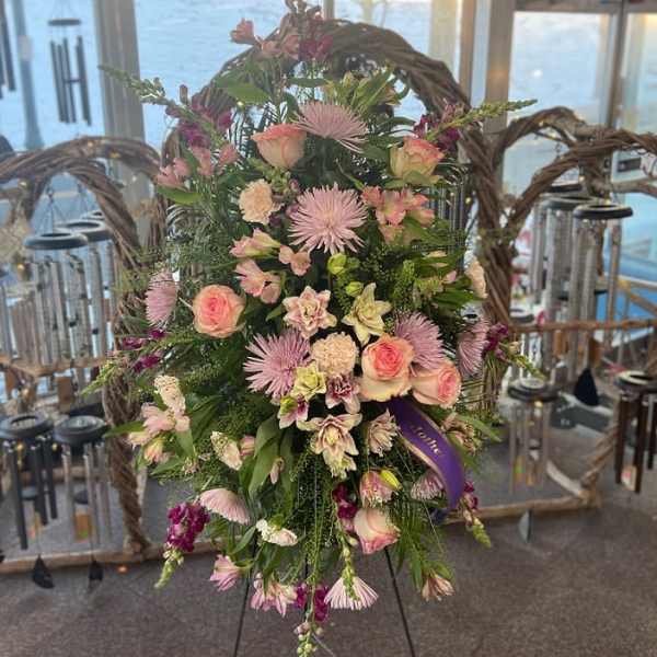 Standing spray of pink roses and mixed flowers on an easel with a purple ribbon