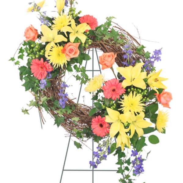 Floral wreath with yellow lilies, orange roses, pink gerberas, and purple accents