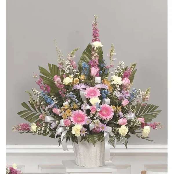 Tall pastel floral arrangement in a white container with ribbon accents