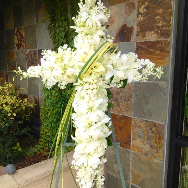 White floral cross on an easel with lilies and orchids