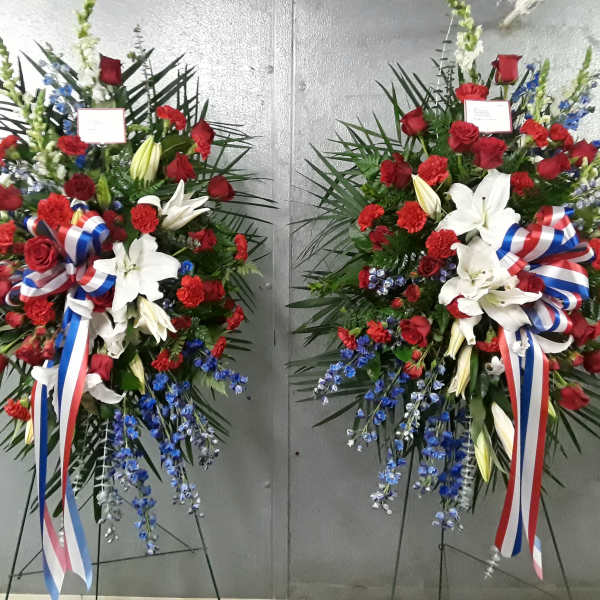 Two large standing floral sprays with red roses, white lilies, and blue accents