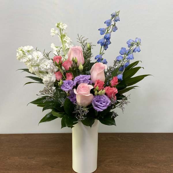 Mixed pink, purple, white, and blue flowers in a white vase