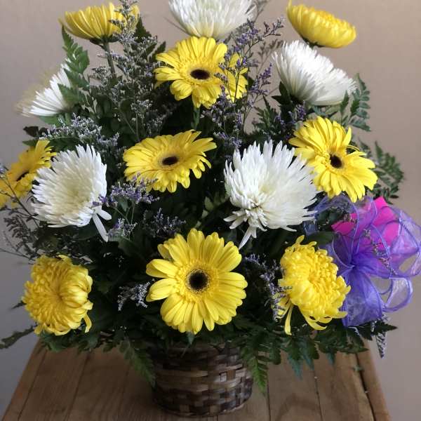 Yellow and white daisy bouquet in a woven basket with a purple ribbon
