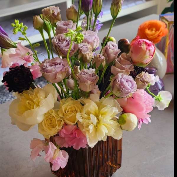Mixed bouquet in an amber glass vase with pink, yellow, purple, and orange blooms.