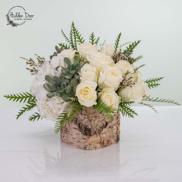 White roses and hydrangeas arranged in a birch bark container