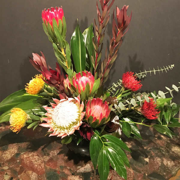 Tropical floral arrangement with pink and red protea in a low vase