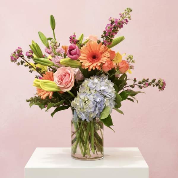 Mixed bouquet in a clear glass vase with pink, orange, and blue blooms