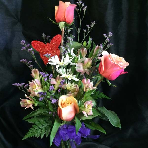 Mixed bouquet of roses and white flowers in a glass vase with a purple ribbon
