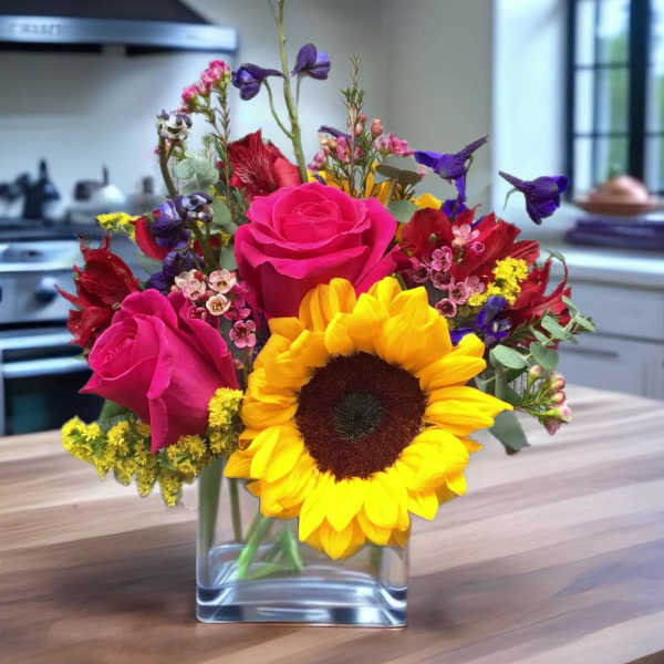 Bright mixed bouquet with sunflowers and pink roses in a clear glass vase