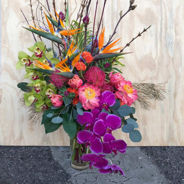 Tall tropical bouquet with orchids, bird of paradise, and pink blooms in a glass vase