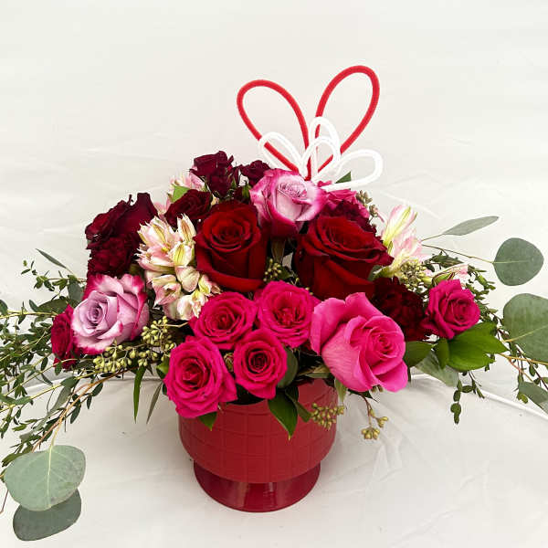 Red and pink roses arranged in a red vase with heart picks