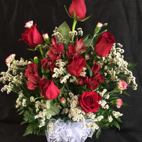 Red roses and red alstroemeria in a clear vase with white ribbon