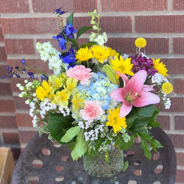 Mixed bouquet in a glass vase with pink lily, blue hydrangea, and yellow daisies