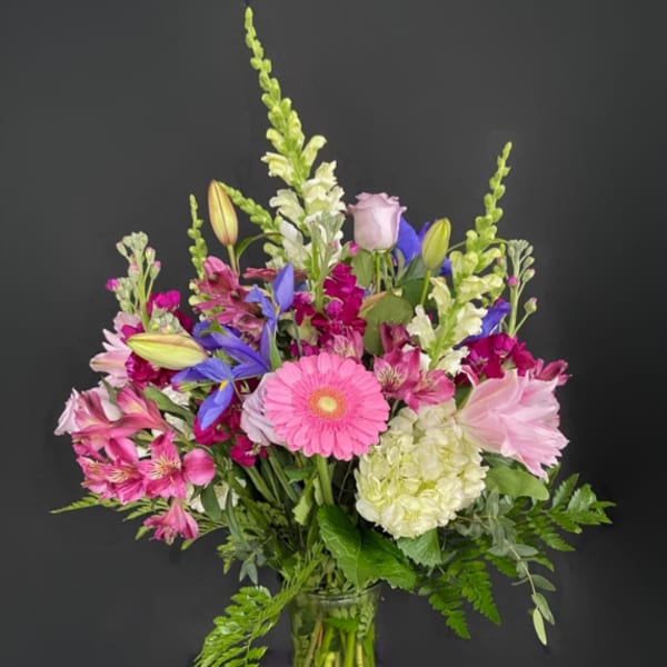 Mixed pink, purple, and white flowers arranged in a glass vase