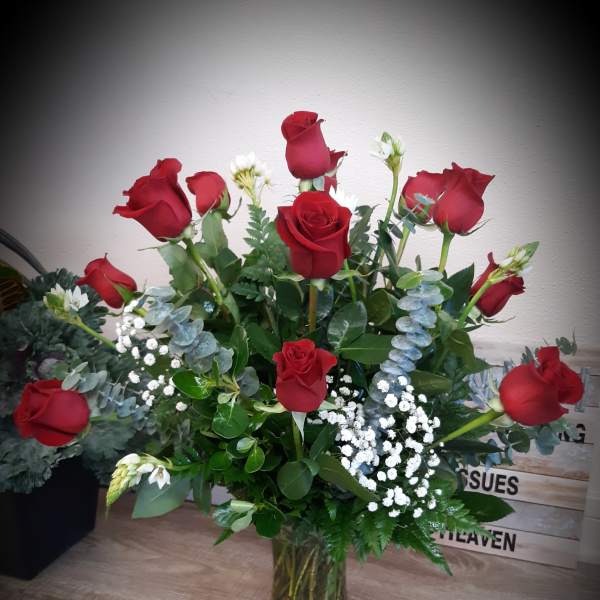 Tall arrangement of red roses with white filler flowers in a clear glass vase