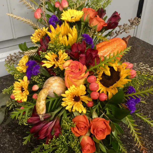 Autumn floral arrangement with sunflowers, orange roses, and a pumpkin accent