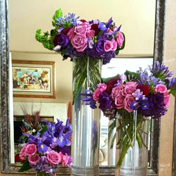 Three purple and pink floral arrangements in tall glass vases
