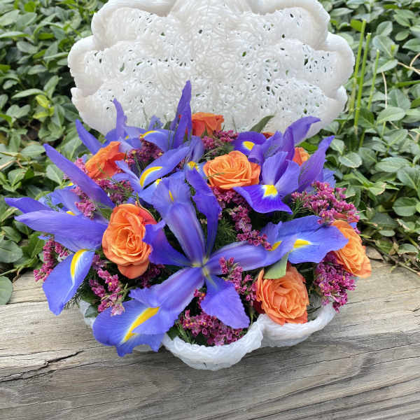 Bouquet of orange roses and purple irises in a white woven basket