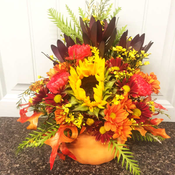 Autumn floral arrangement in a pumpkin-shaped container with sunflowers and daisies