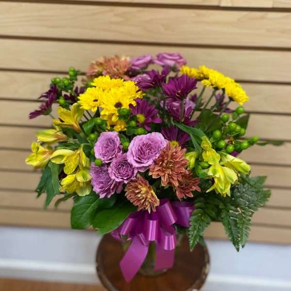 Mixed bouquet of purple, yellow, and pink flowers in a vase with a ribbon