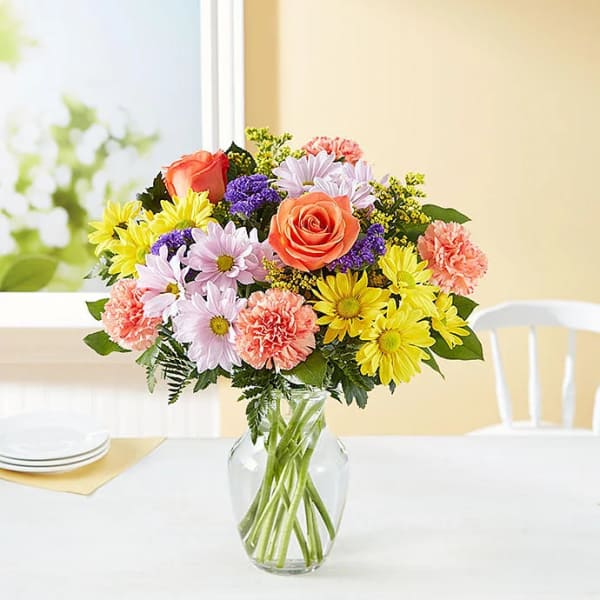 Mixed bouquet of roses, daisies, and carnations in a glass vase