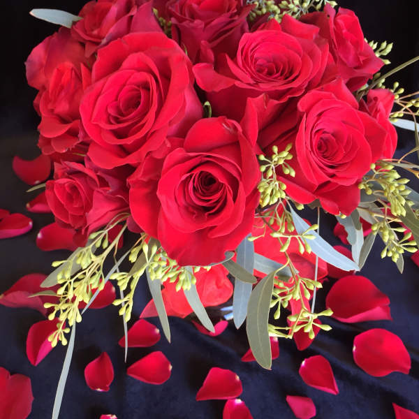 Bouquet of red roses with scattered rose petals on a dark background