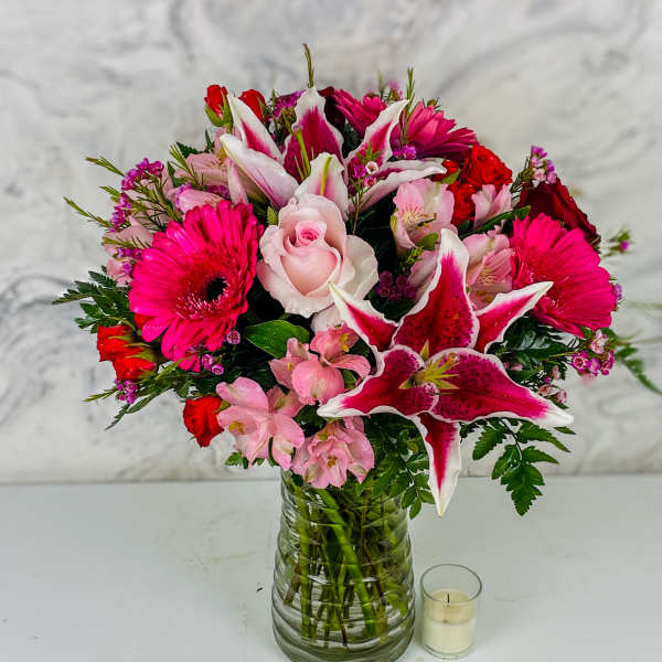 Pink and red mixed bouquet in a glass vase with a small candle beside it