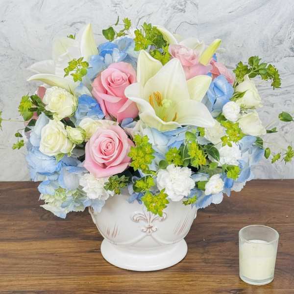 Pink roses and white lilies arranged in a white vase with blue flowers