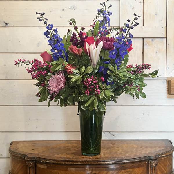Mixed bouquet in a tall glass vase with blue, pink, and white flowers