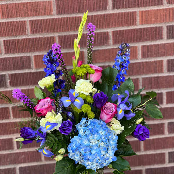 Mixed bouquet of blue hydrangea, pink roses, and purple flowers in a glass vase