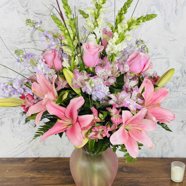 Pink lilies and roses arranged in a frosted glass vase