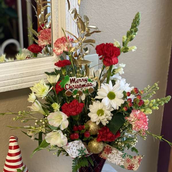 Christmas floral arrangement in a red vase with a Merry Christmas pick