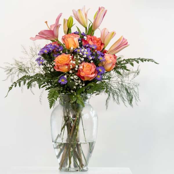 Mixed bouquet of pink lilies and orange roses in a glass vase