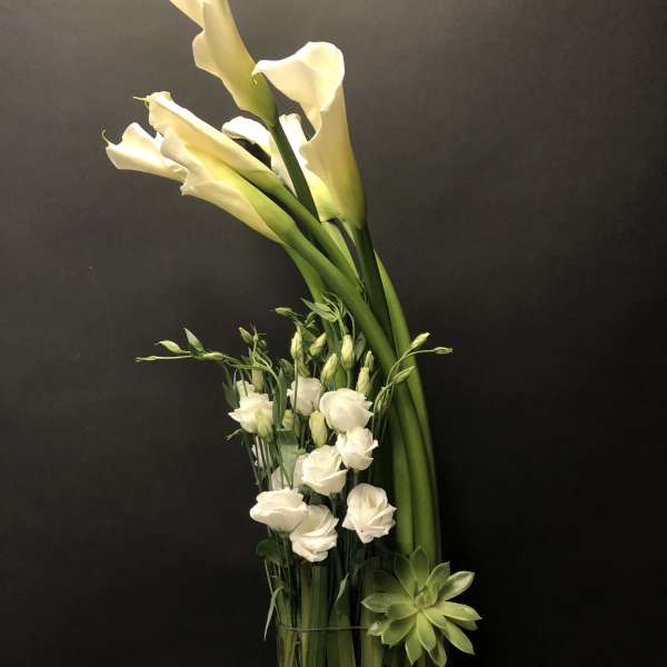 White calla lilies and small white blooms in a glass vase