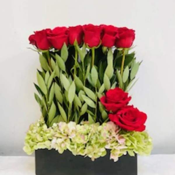Red roses arranged in a black rectangular box with pale hydrangeas